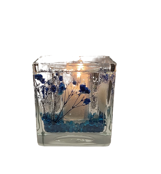Bougie allumée dans un photophore en verre transparent avec des motifs bleus et des perles bleues à l'intérieur.
