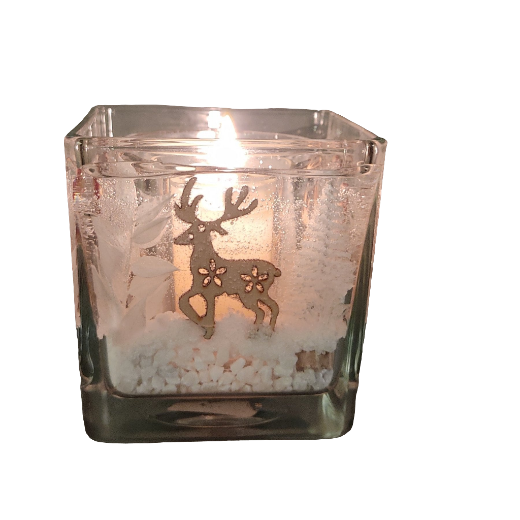 Photophore en verre carré avec un cerf, une bougie allumée à l’intérieur et des petites décorations blanches au fond, évoquant une ambiance hivernale et chaleureuse.