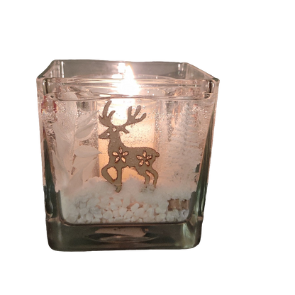 Photophore en verre carré avec un cerf, une bougie allumée à l’intérieur et des petites décorations blanches au fond, évoquant une ambiance hivernale et chaleureuse.